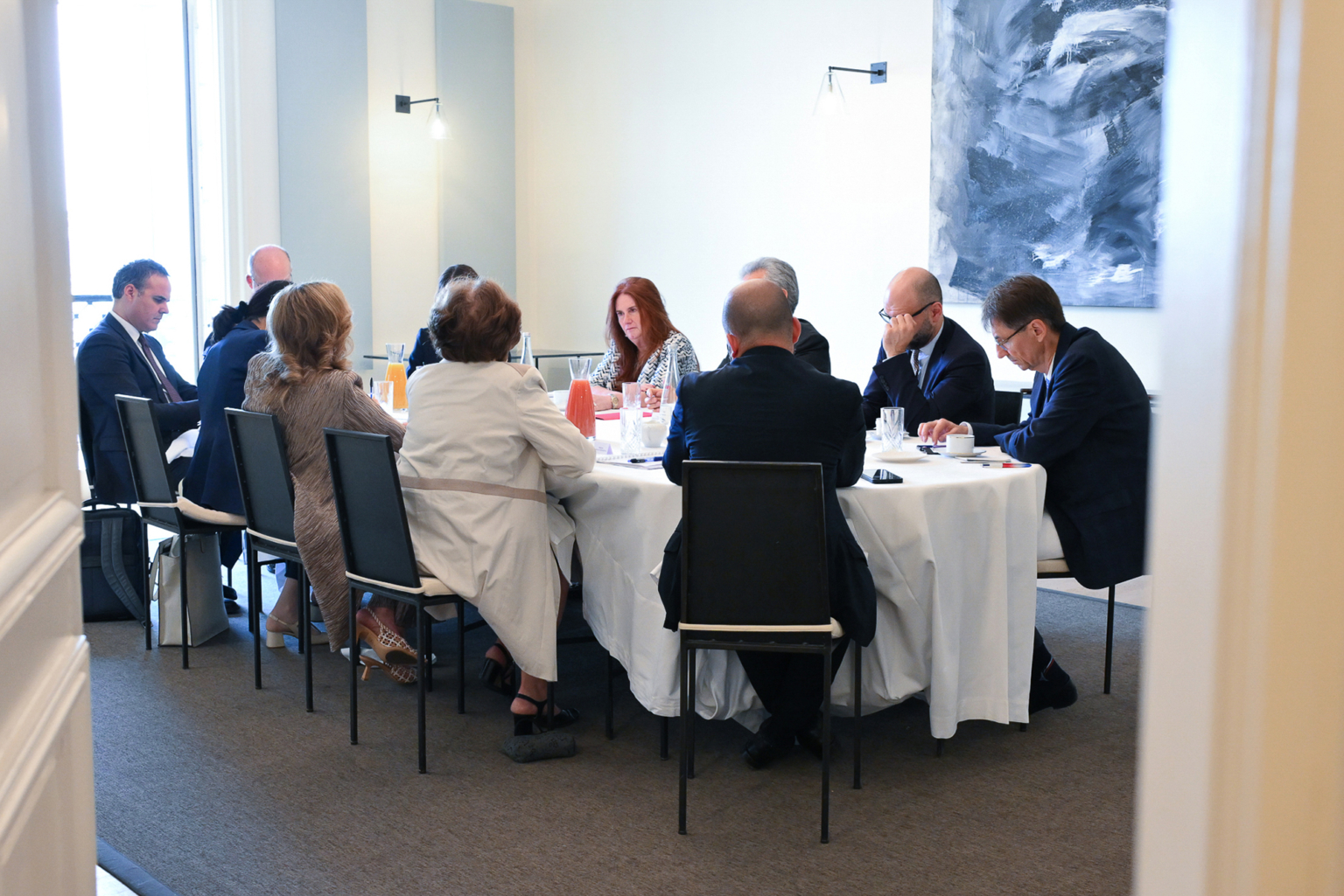 Un groupe de personnes en tenue de travail est assis autour d'une table ronde dans une salle de réunion et discute. La table est recouverte d'une nappe blanche et contient des boissons et des documents. Photographe Xavier Granet